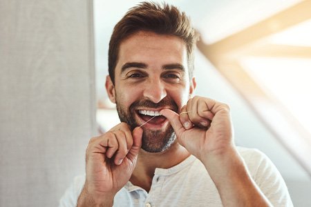 Man smiling while flossing his teeth in bathroom
