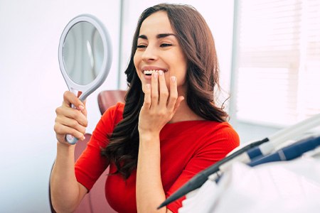 Woman smiling at reflection in handheld mirror