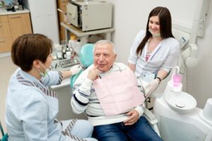 Older dental patient pointing towards mouth and asking dentist a question.